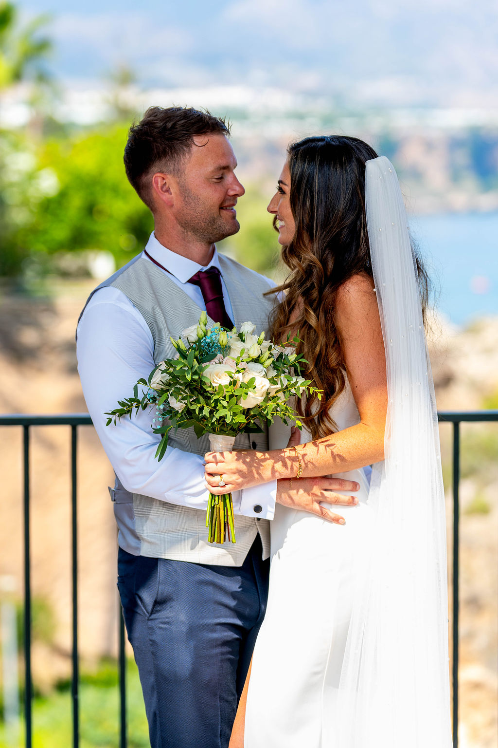 Irish Bride and groom holding bouquet at Balcón de Europa Nerja Spain with coastal view in background.