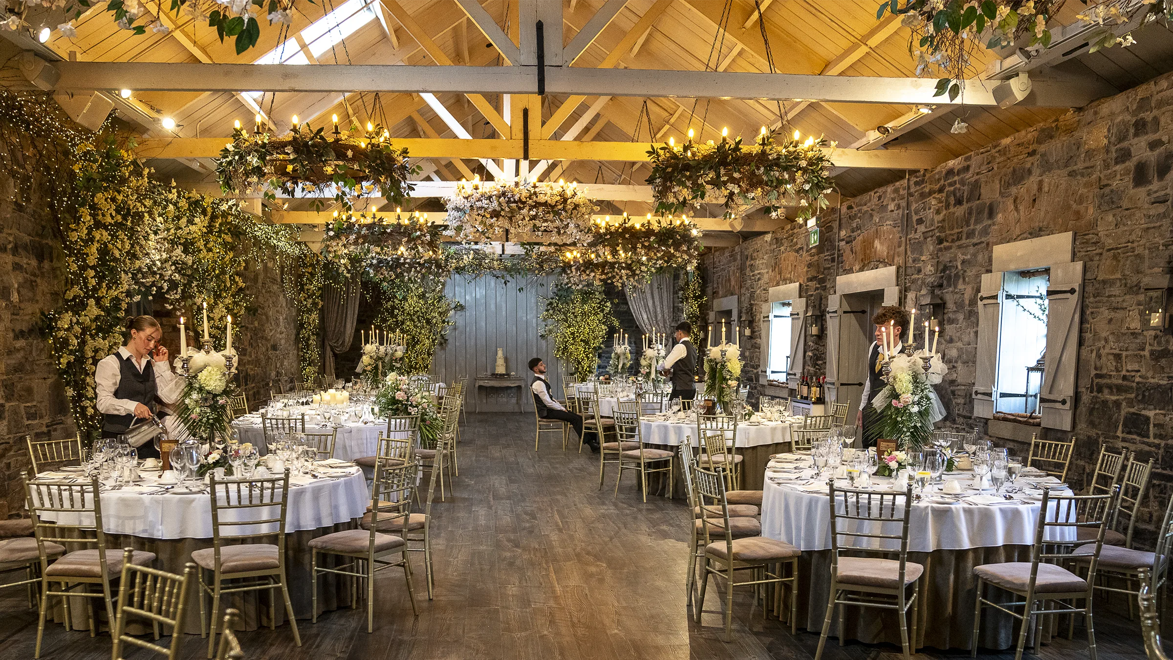 Ballymagarvey Village wedding reception room with stone walls, timber beams, greenery and dressed tables