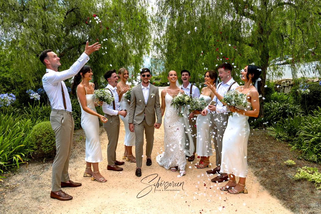 Beautiful bride and groom surrounded by their bridal party, throwing confetti joyfully as they walk through the elegant surroundings of Hotel Cortijo Bravo in Velez Malaga, Spain. Captured by Dougie Farrelly, the recommended photographer for Cortijo Bravo Weddings