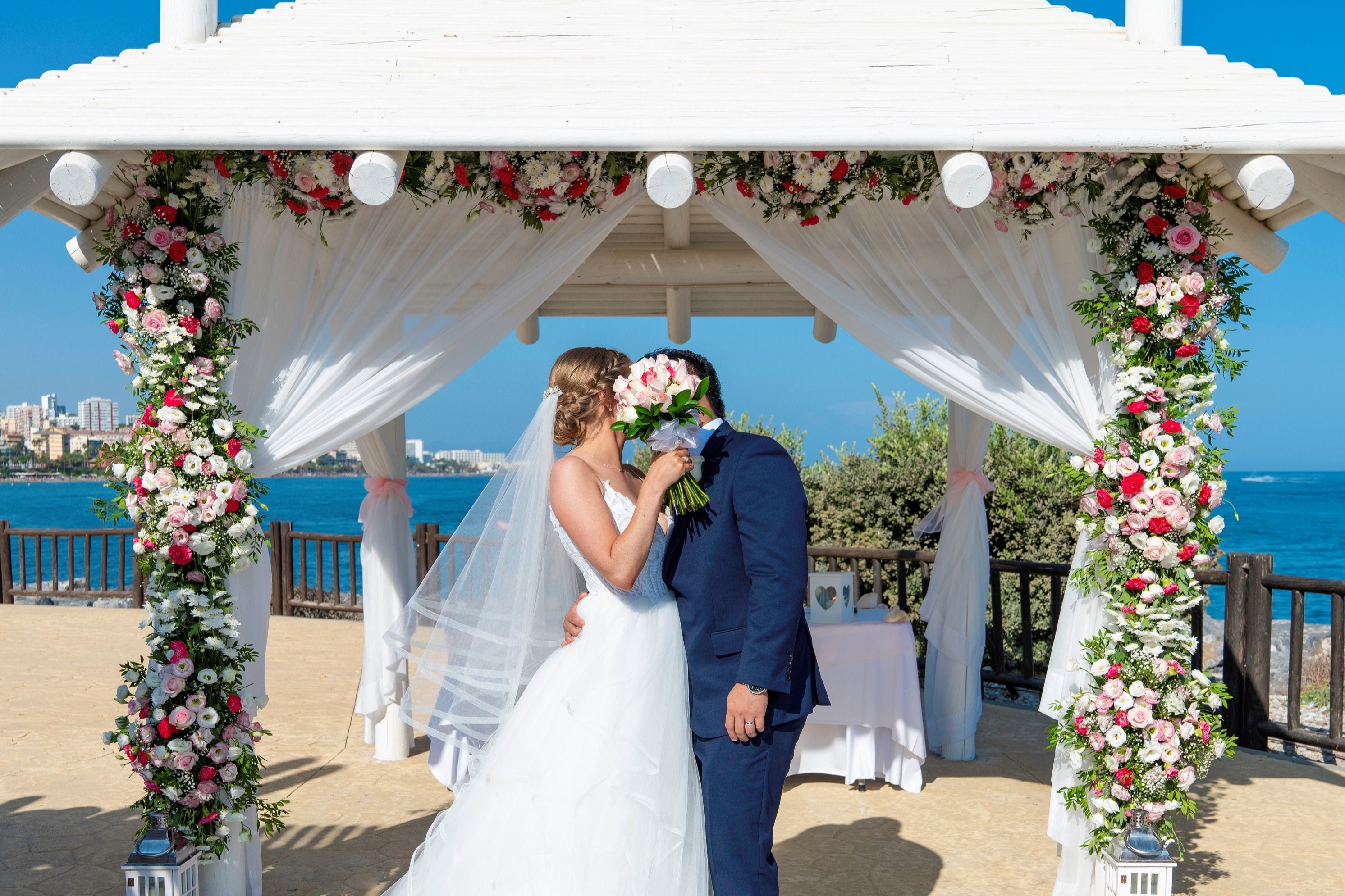 Bride and groom kissing under floral ceremony arch at Sunset Beach Club Benalmádena Costa del Sol Spain with sea view