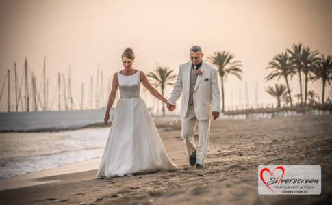 A peaceful stroll at golden hour as the bride and groom walk hand-in-hand along the shores of Marbella, with sailboats and palm trees setting the scene.
© All Rights Reserved Dougie Farrelly Silverscreen.ie Bride and groom walking hand-in-hand along Marbella beach at sunset with sailboats and palm trees in the background