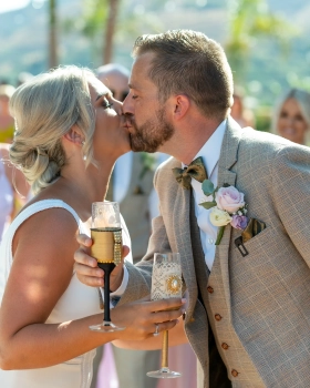 Rachel Smyth and George McMahon kissing while holding champagne glasses during their wedding celebrations in Nerja, Spain.