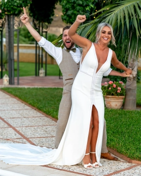 Rachel Smyth and George McMahon celebrating with their arms raised during their wedding in Nerja, Spain.