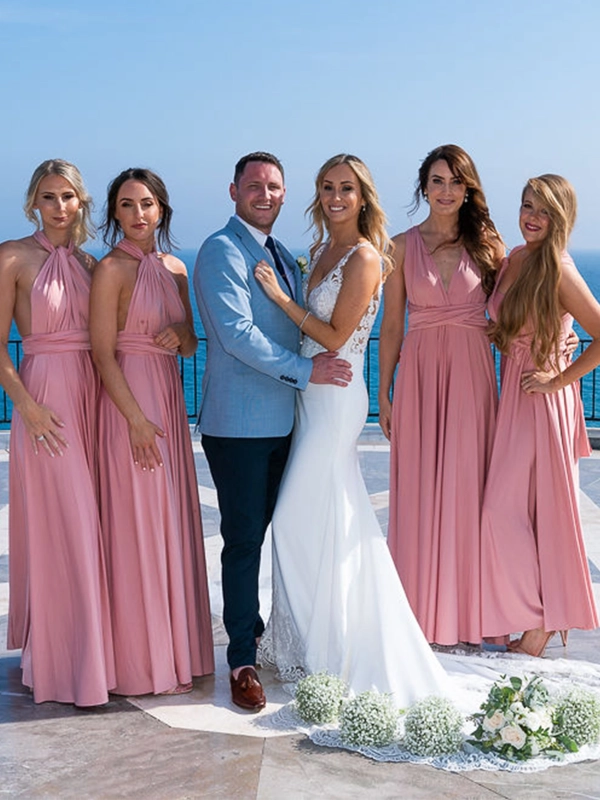 Ruth and James posing with four bridesmaids in pink dresses on a seaside terrace overlooking the Mediterranean Sea.